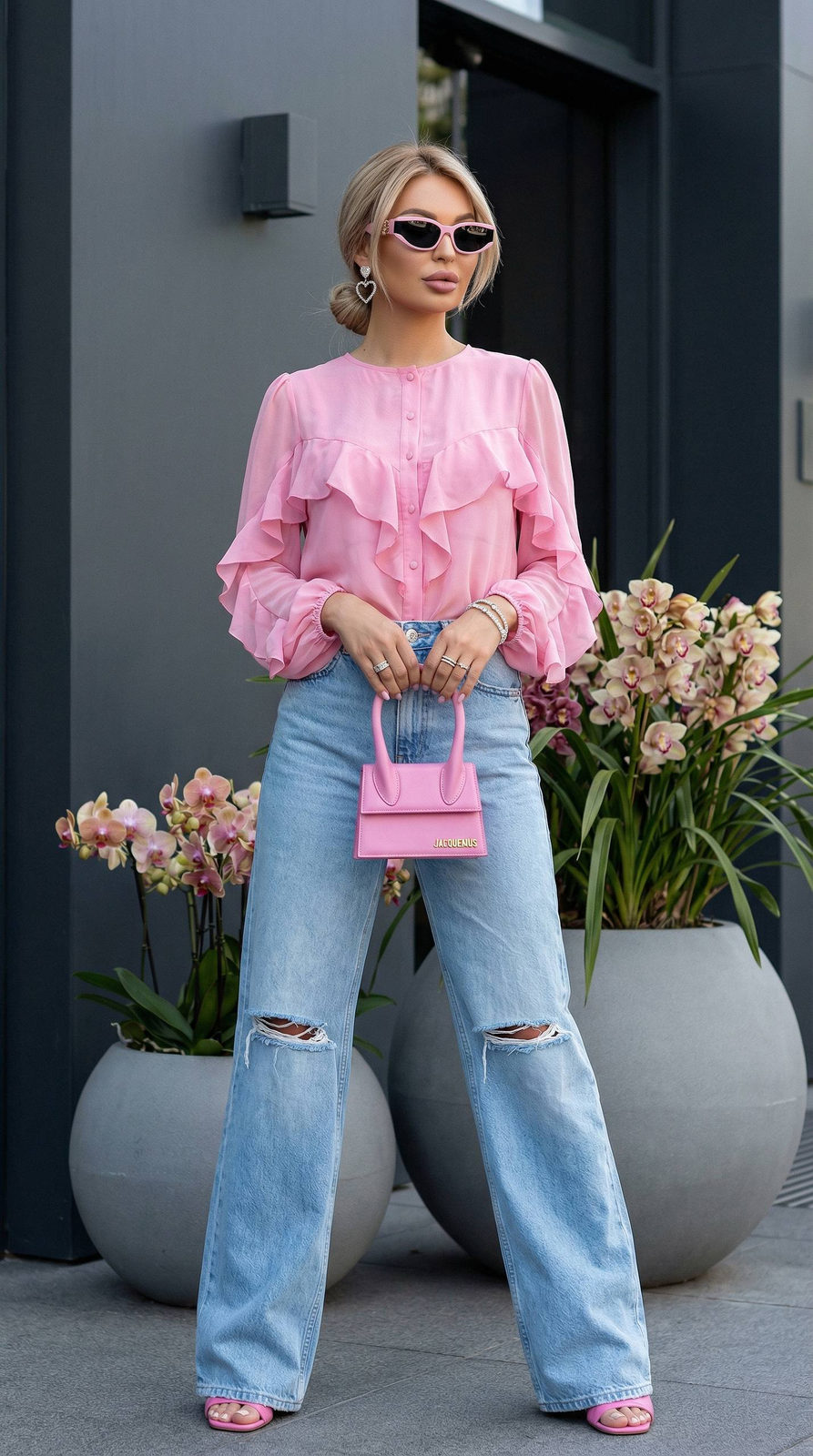 Cinematic portrait of a girl standing by a gray building, holding a small pink Jacquemus bag, surrounded by lush orchids.