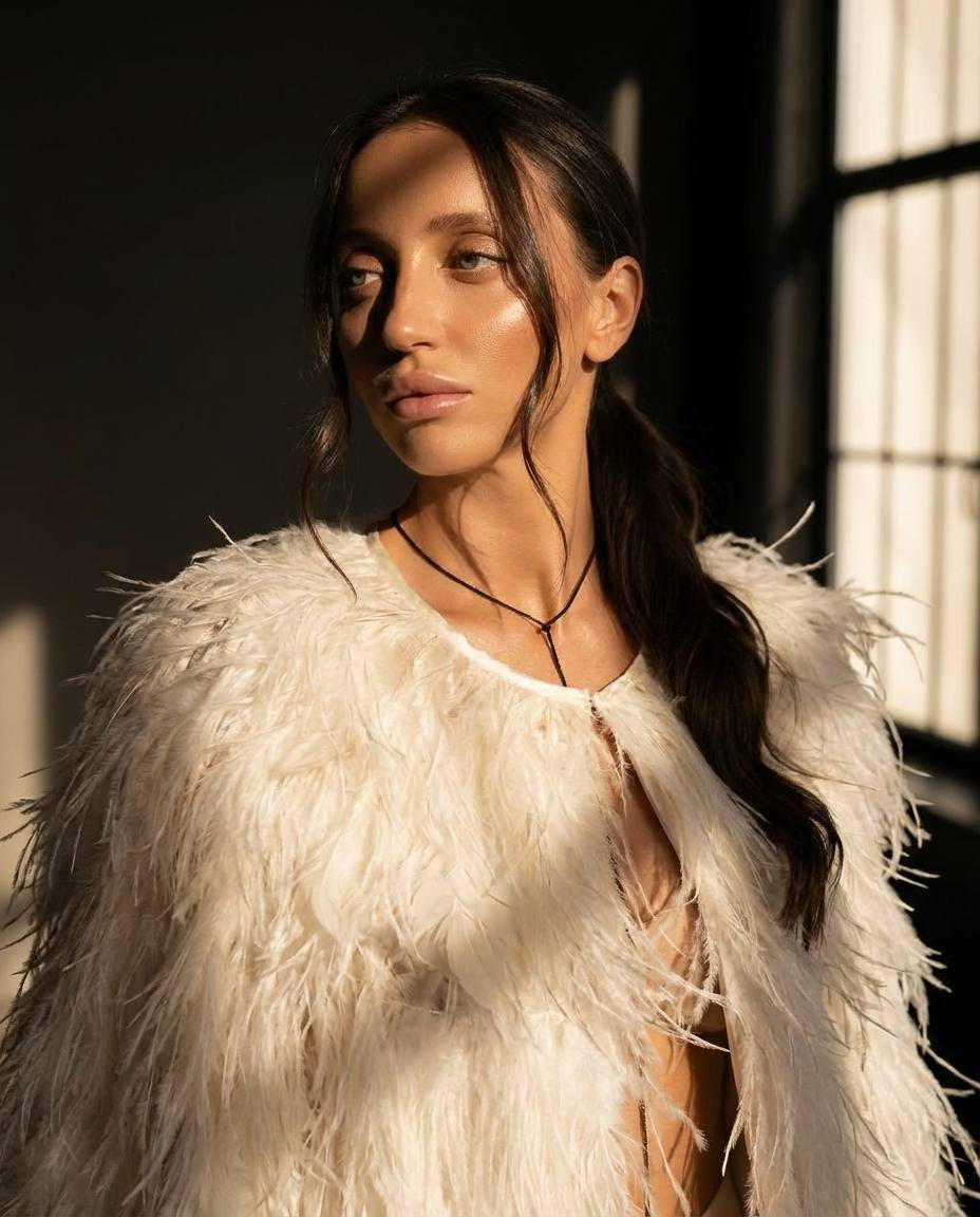 A model in a snow-feather wrap striking a pose in a dark studio with dramatic side lighting and soft shadows.