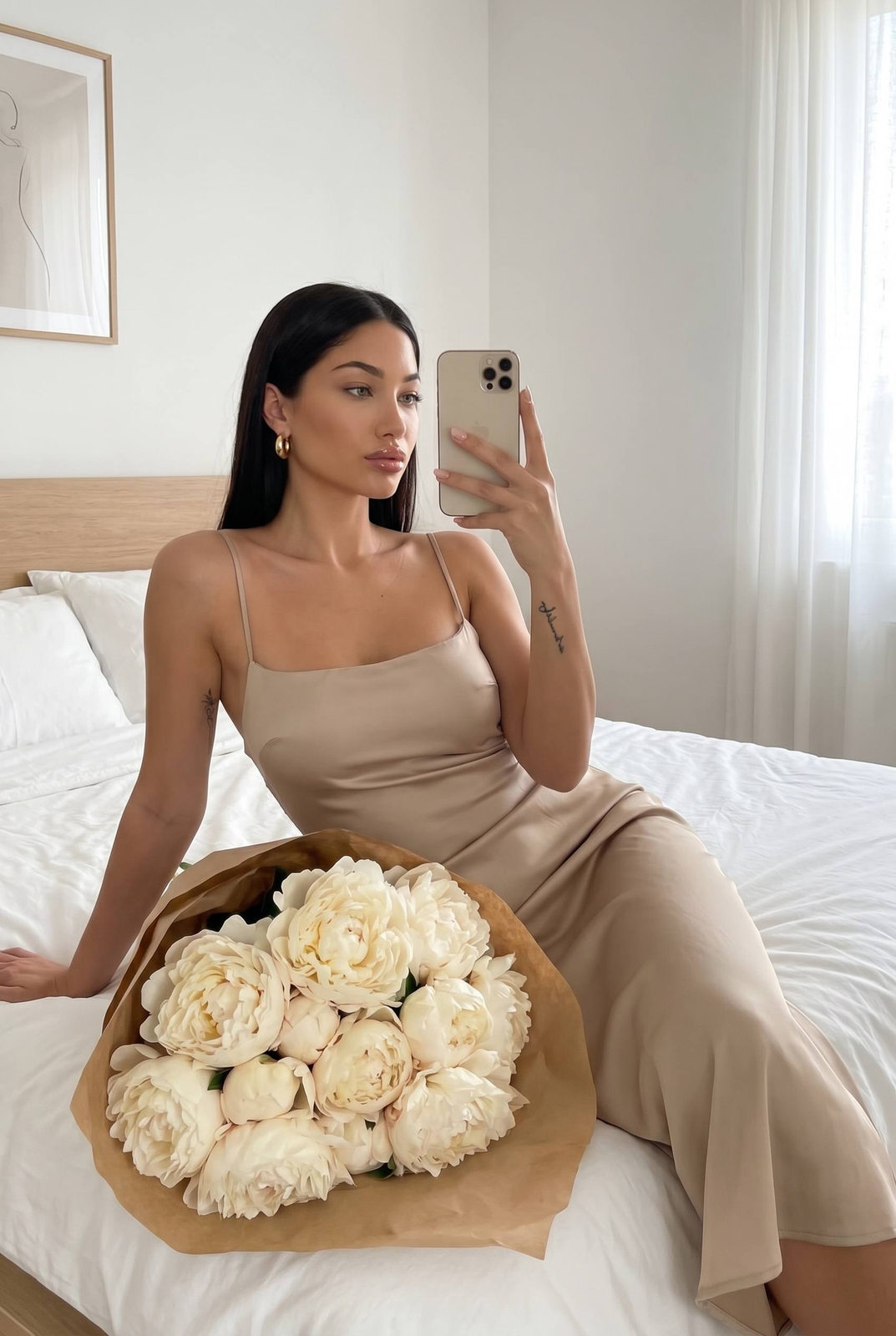 A woman taking a mirror selfie in a minimalist bedroom wearing a beige satin slip dress, holding a smartphone.