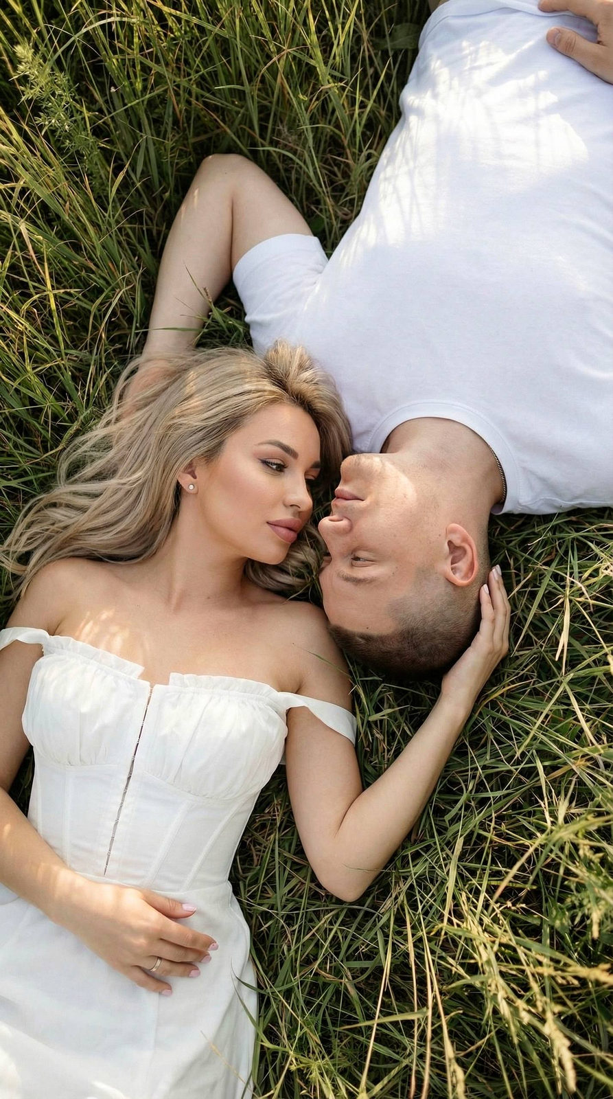 A couple lying in lush grass, gazing at each other with love, sunlight highlighting their features.