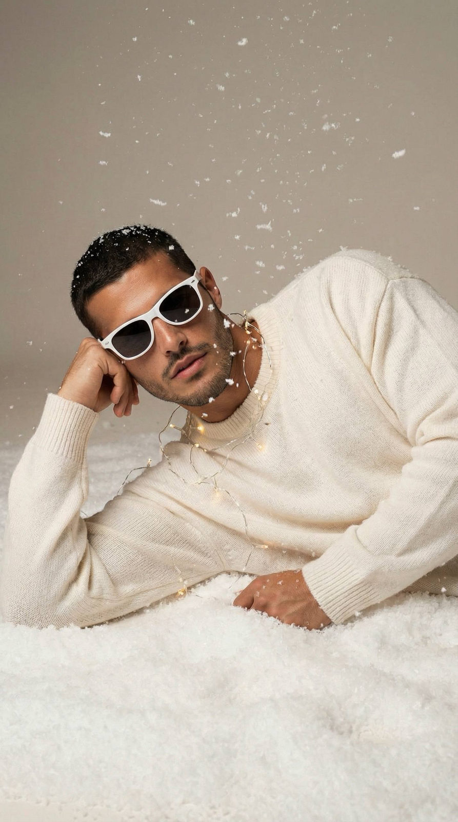 Hyper-realistic studio portrait of a man in a milk-white sweater resting on artificial snow with fairy lights.