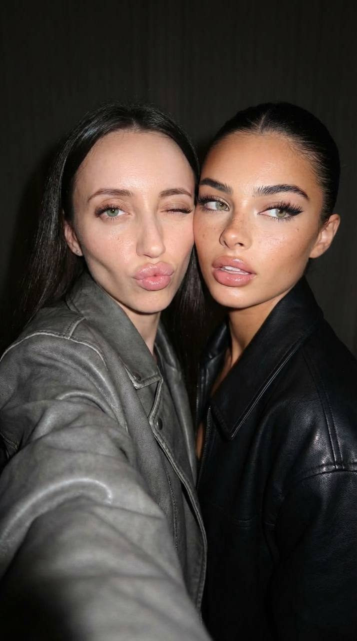 Portrait of two young women posing closely, one in a gray oversized jacket and the other in a black oversized jacket with confident expressions.