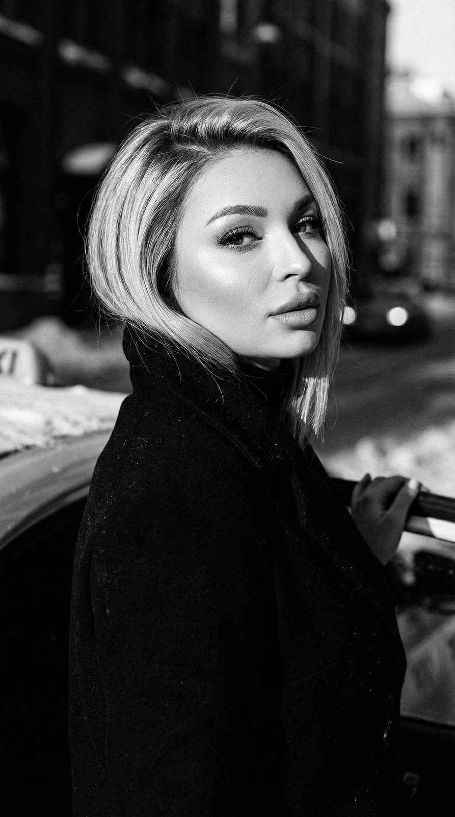 Cinematic close-up of a woman in a winter city, illuminated by sunlight, leaning against a taxi with a high-collared coat.