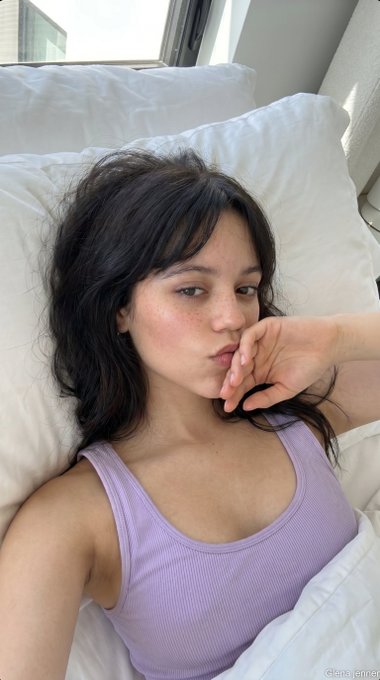 Close-up selfie of person in light lavender tank top lying in bed