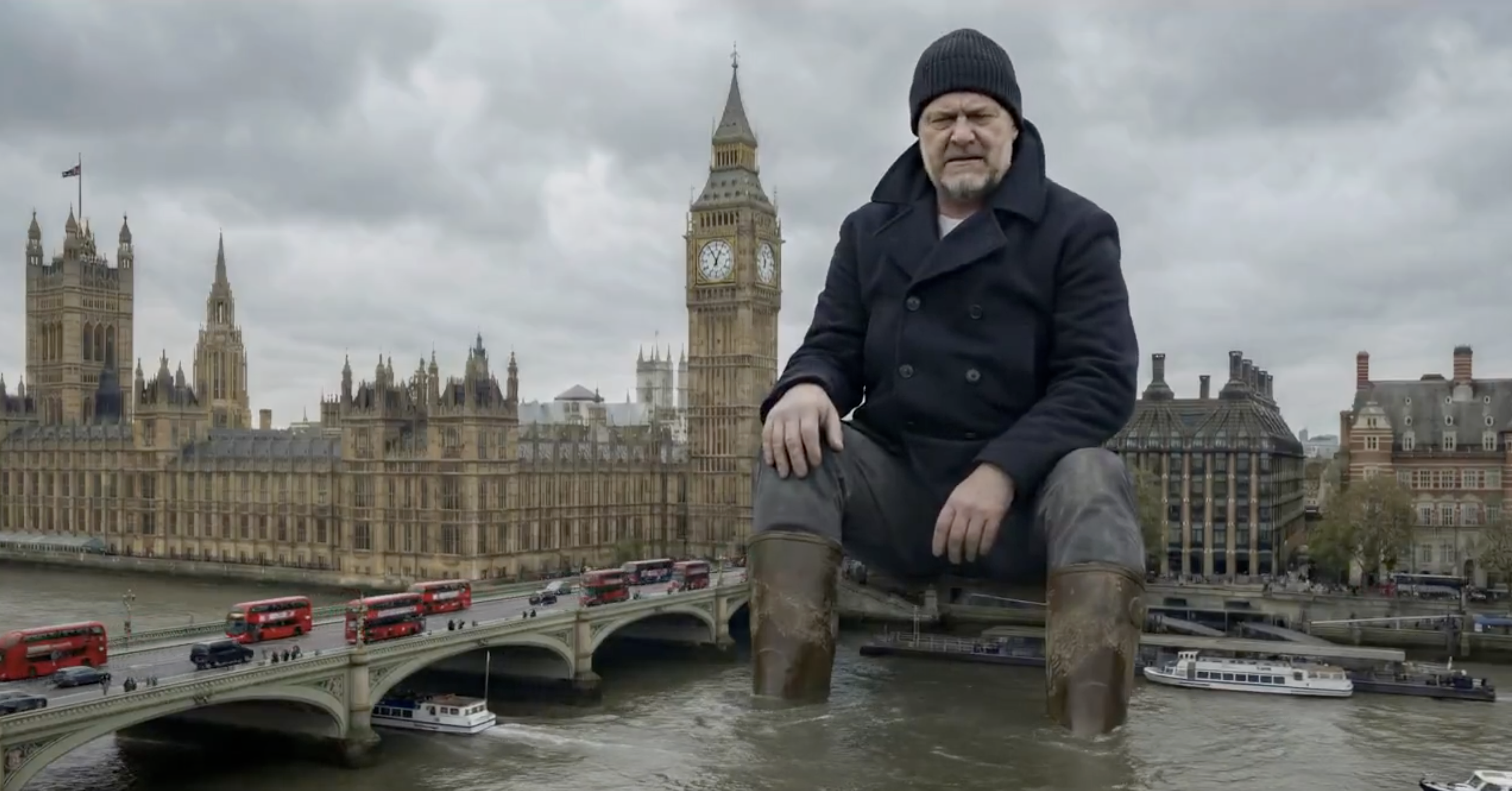 Photorealistic image of a giant man in a peacoat sitting by the River Thames, with Big Ben in the background and tiny buses around his legs.