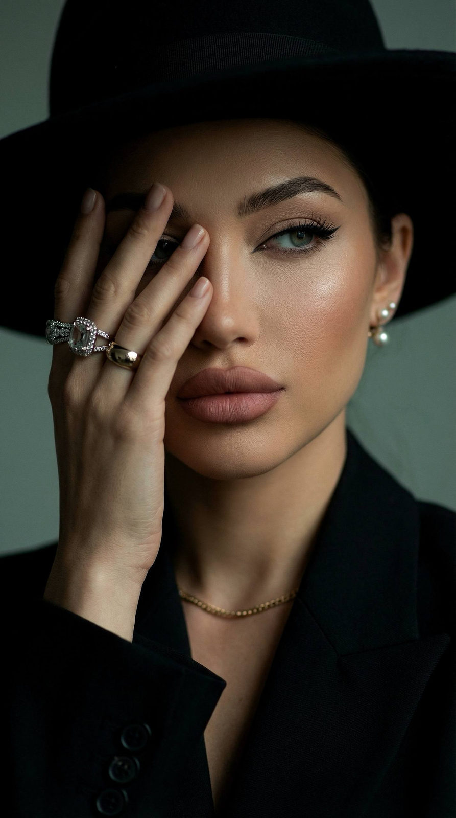 A close-up portrait showing a model in dramatic lighting, with a black wide-brimmed hat casting shadows across her face.