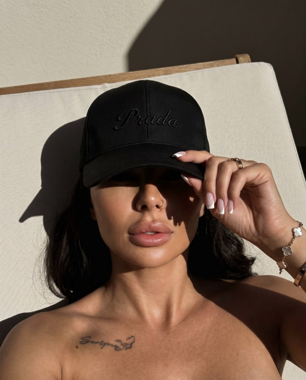 Close-up portrait of a girl in a black baseball cap lying on a light lounge chair from above, showcasing soft skin tones and shadows.
