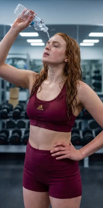 Athletic woman with red hair in maroon Adidas outfit cooling down in gym.