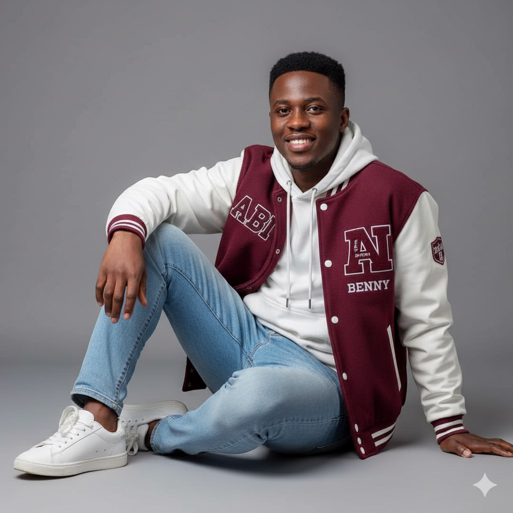 Portrait of a young African entrepreneur in a burgundy university jacket, seated casually against a neutral grey background.