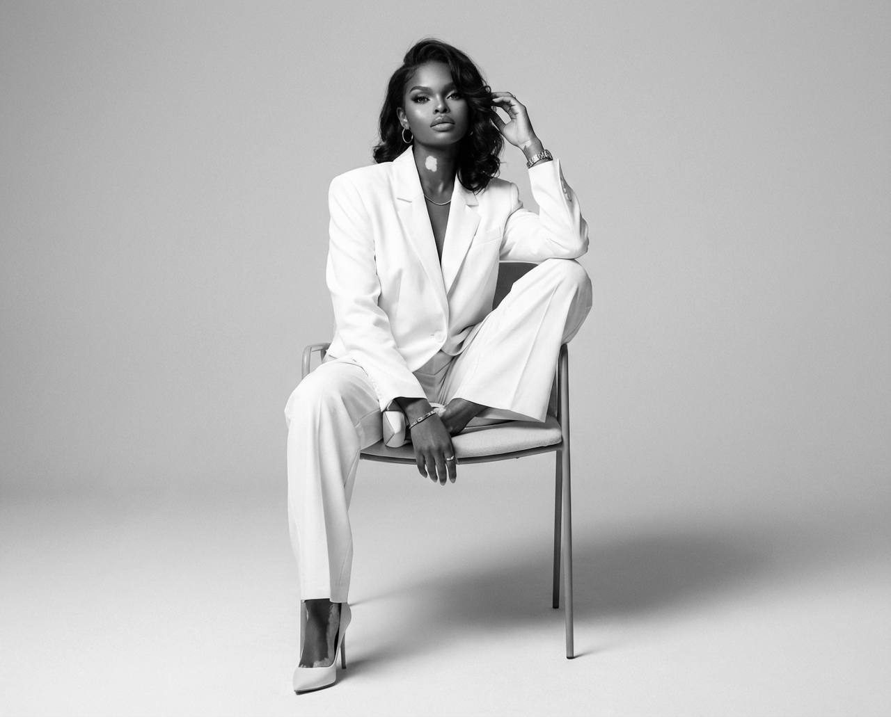 Photorealistic studio fashion portrait of a person in a crisp oversized blazer posing on a modern chair.