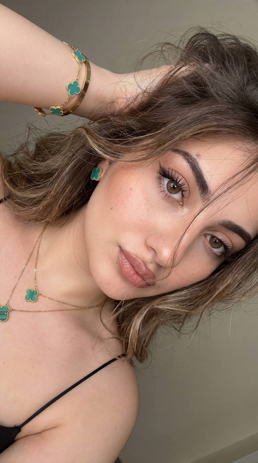 Close-up selfie of a woman with layered hair, soft focus on her face, light makeup, and muted background.