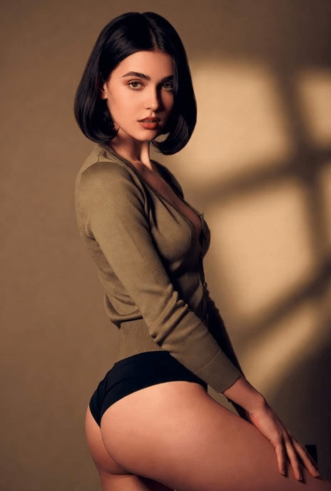 Model in olive green knit cardigan poses against a beige wall, dramatic shadows highlighting their features.