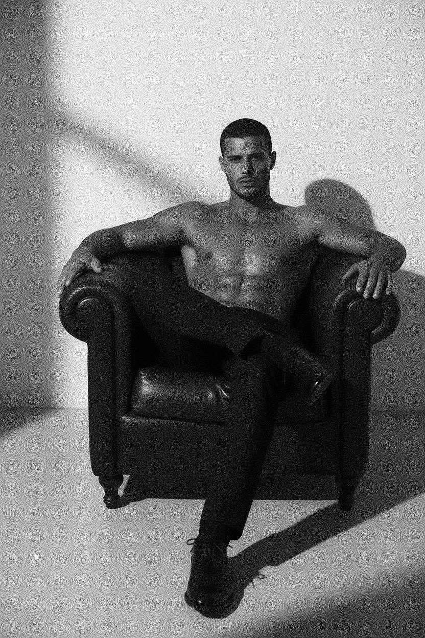 A minimalist black and white portrait of a man sitting casually in a dark leather chair, showcasing a confident pose.