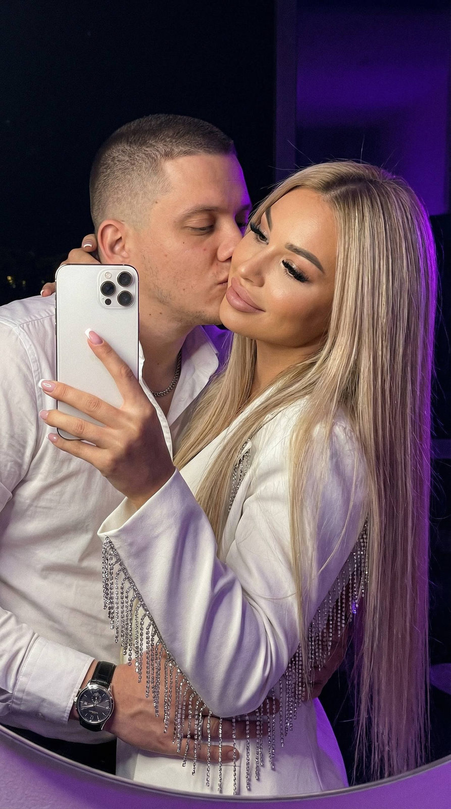 Cinematic close-up of a couple sharing a mirror selfie with purple night lighting, emphasizing their romantic connection.