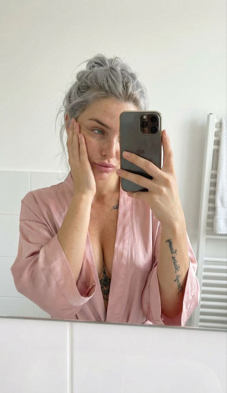 A person wearing a soft pink silk dressing gown in a bright bathroom, captured mid-gesture with natural folds and sheen of the fabric.