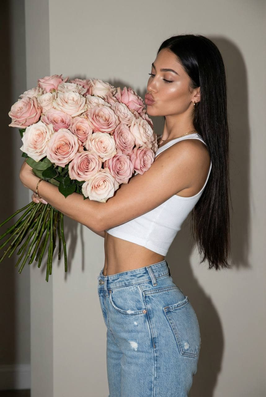 A woman in profile holding a large bouquet of soft pink roses, set against a neutral indoor background with ambient lighting.