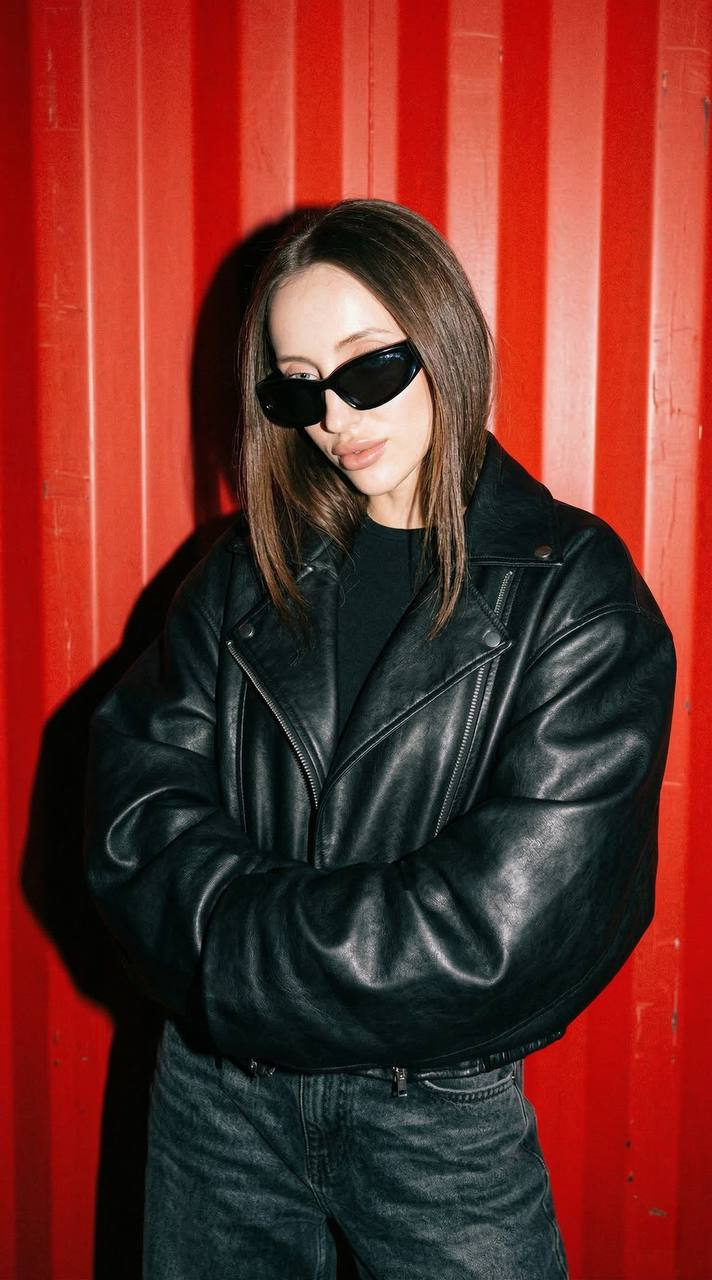 Extreme close-up portrait of a stylish woman in a black leather jacket standing in front of a bright red metal wall.