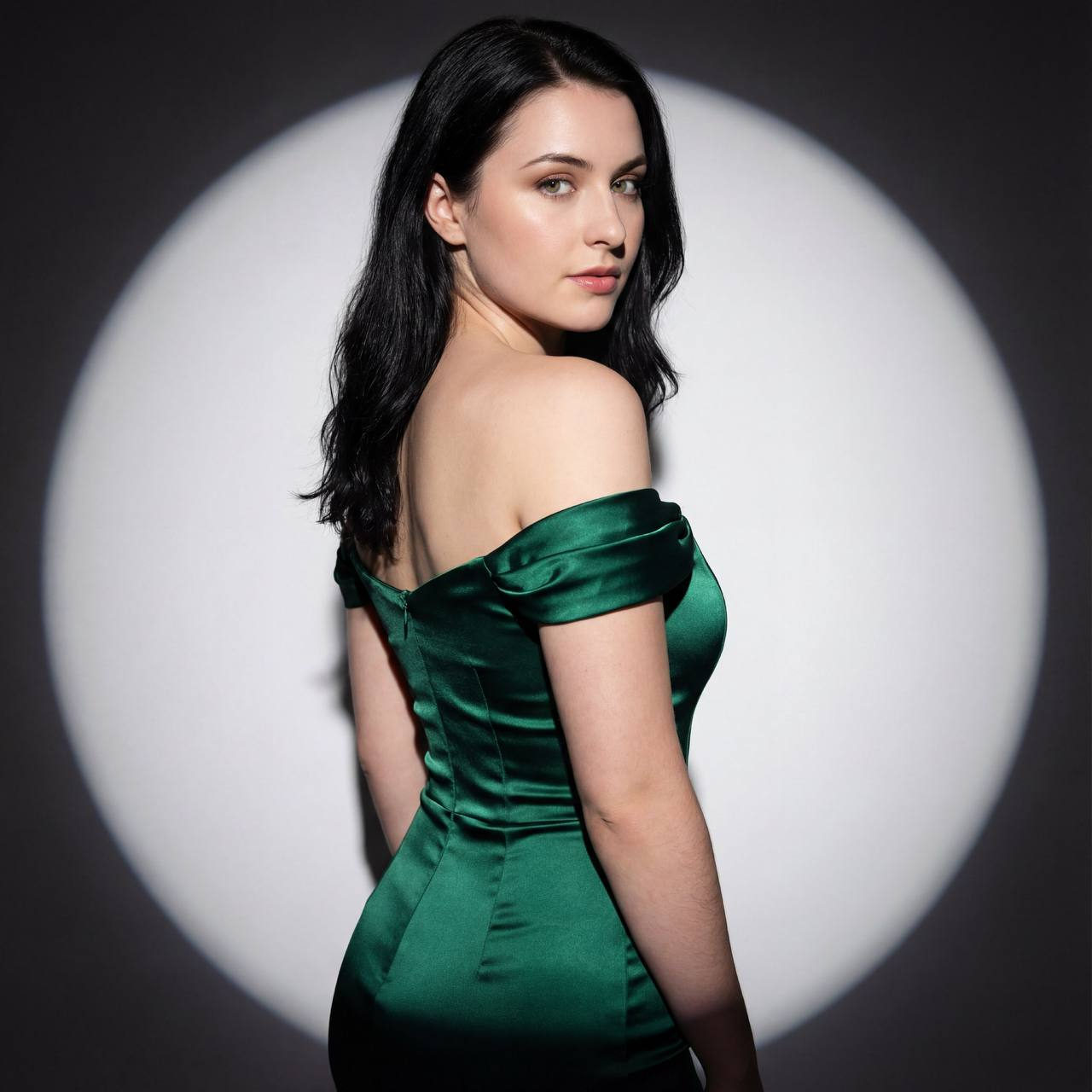 Close-up portrait of a woman in a green satin dress, looking over her shoulder with sensual confidence against a dark gray background.