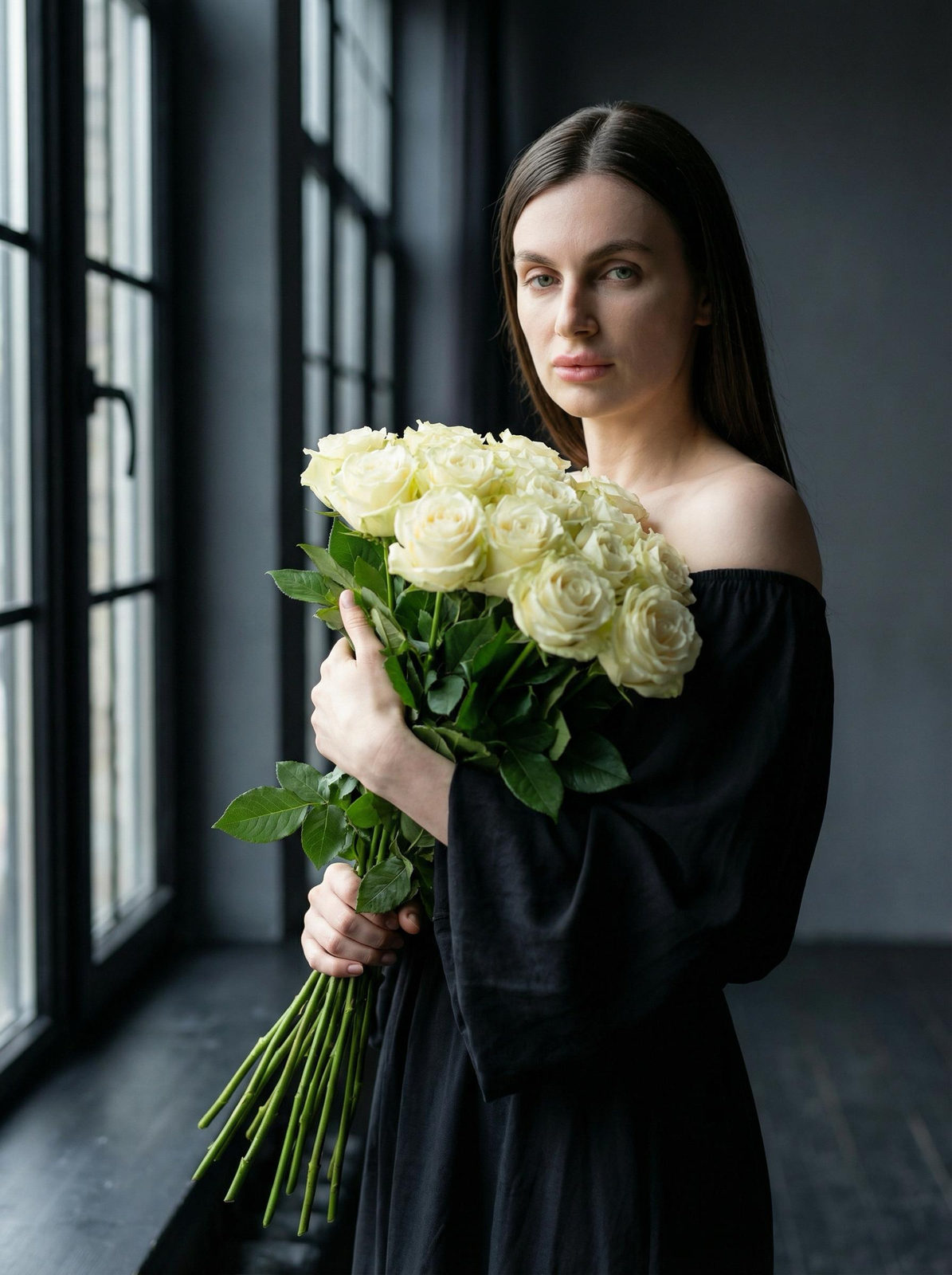 A woman holding a large bouquet of white roses in a softly lit interior, with her gaze directed at the camera.