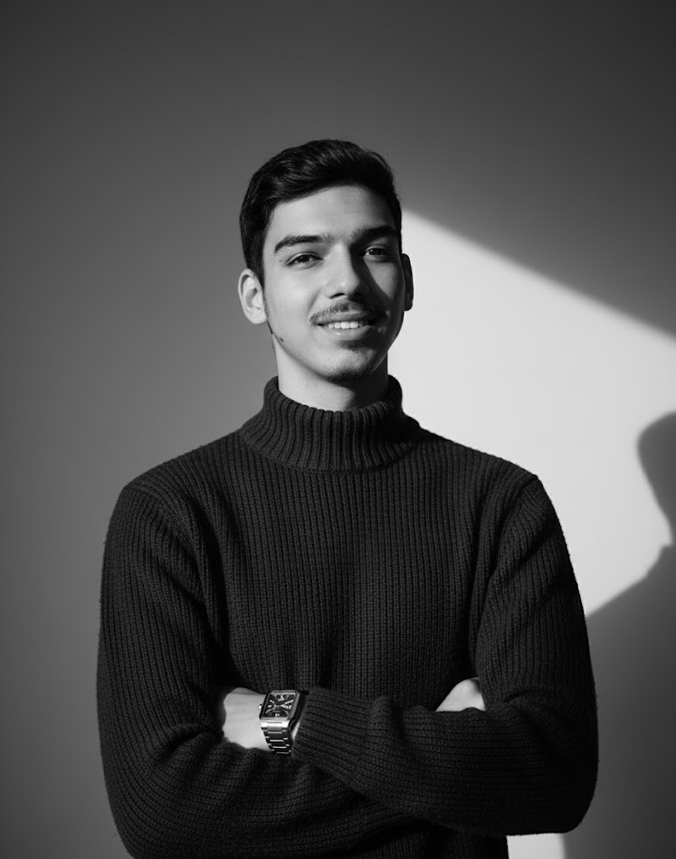 Retrato de homem com suéter preto em fundo cinza, braços cruzados, sorrindo e usando relógio quadrado.