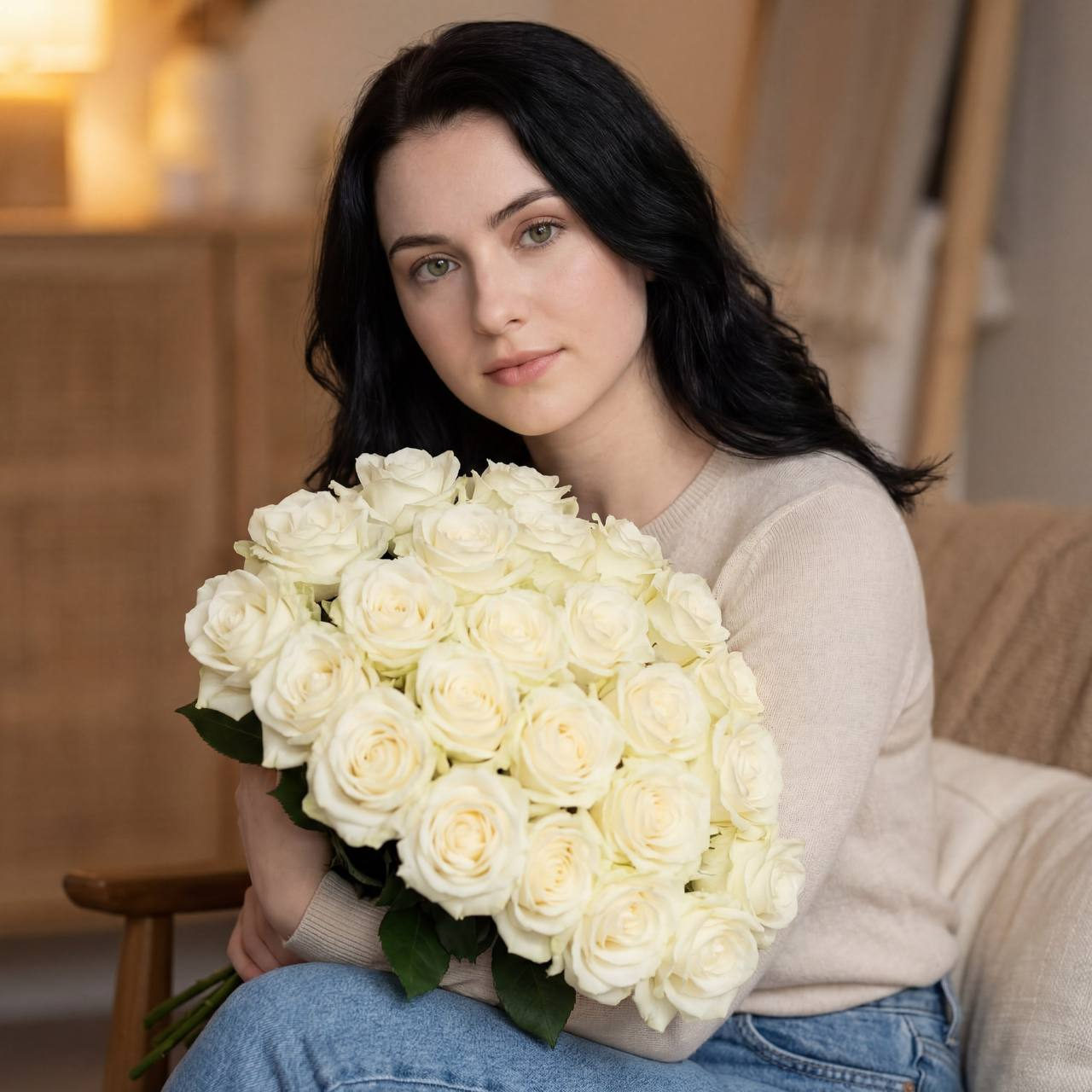 A woman with long hair in a light top sits gracefully with a bouquet of roses.