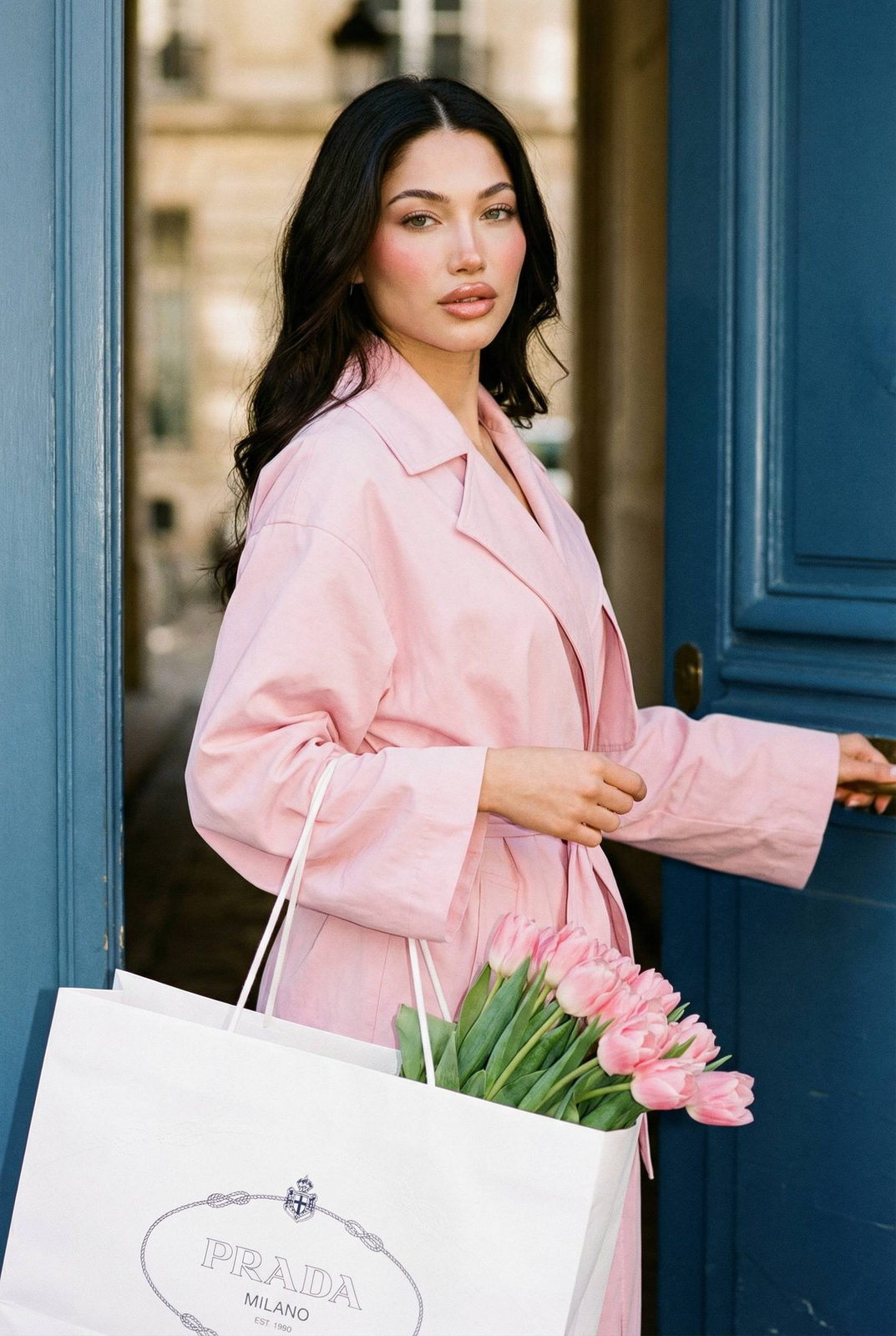 Woman in a pastel pink coat holding tulips by a blue door