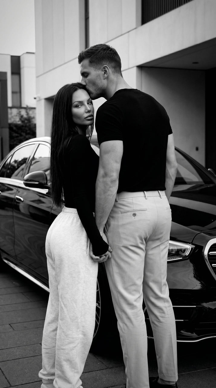 Couple standing beside a vintage car in black and white, capturing a moment filled with love and affection.