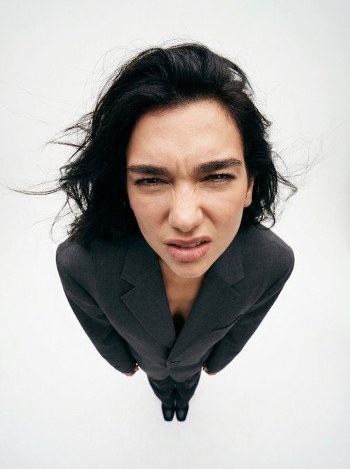 Close-up of a windblown woman's face in a 90s suit, distorted features against a white background.