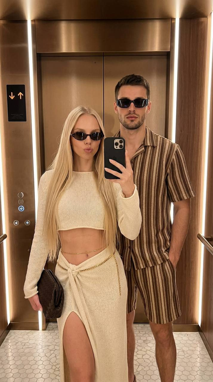 Stylish couple taking a full-length selfie in an elevator, showcasing warm neutrals with a modern ambiance.
