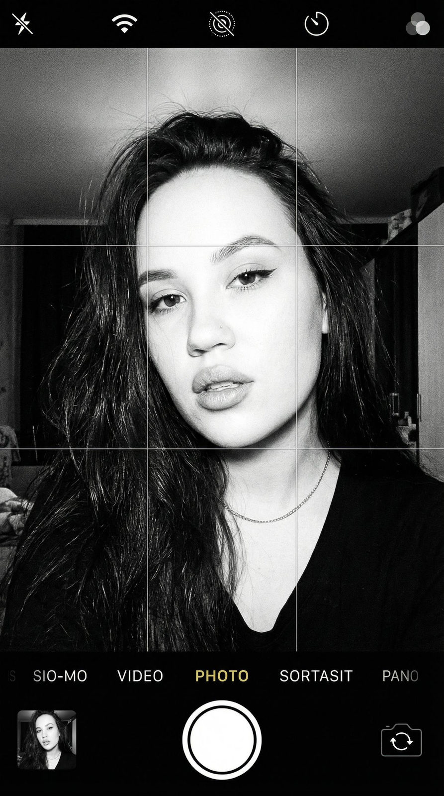 Black and white selfie with iPhone camera UI, girl with relaxed expression, slightly parted lips, high contrast with film grain effect.