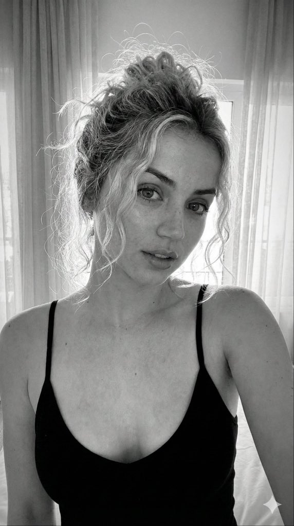 Close-up portrait of a young Caucasian woman with textured blonde curly hair in a messy bun, soft freckles on her face, and direct eye contact.