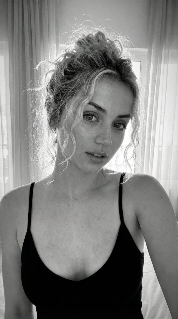 Close-up portrait of a young Caucasian woman with textured blonde curly hair in a messy bun, soft freckles on her face, and direct eye contact.