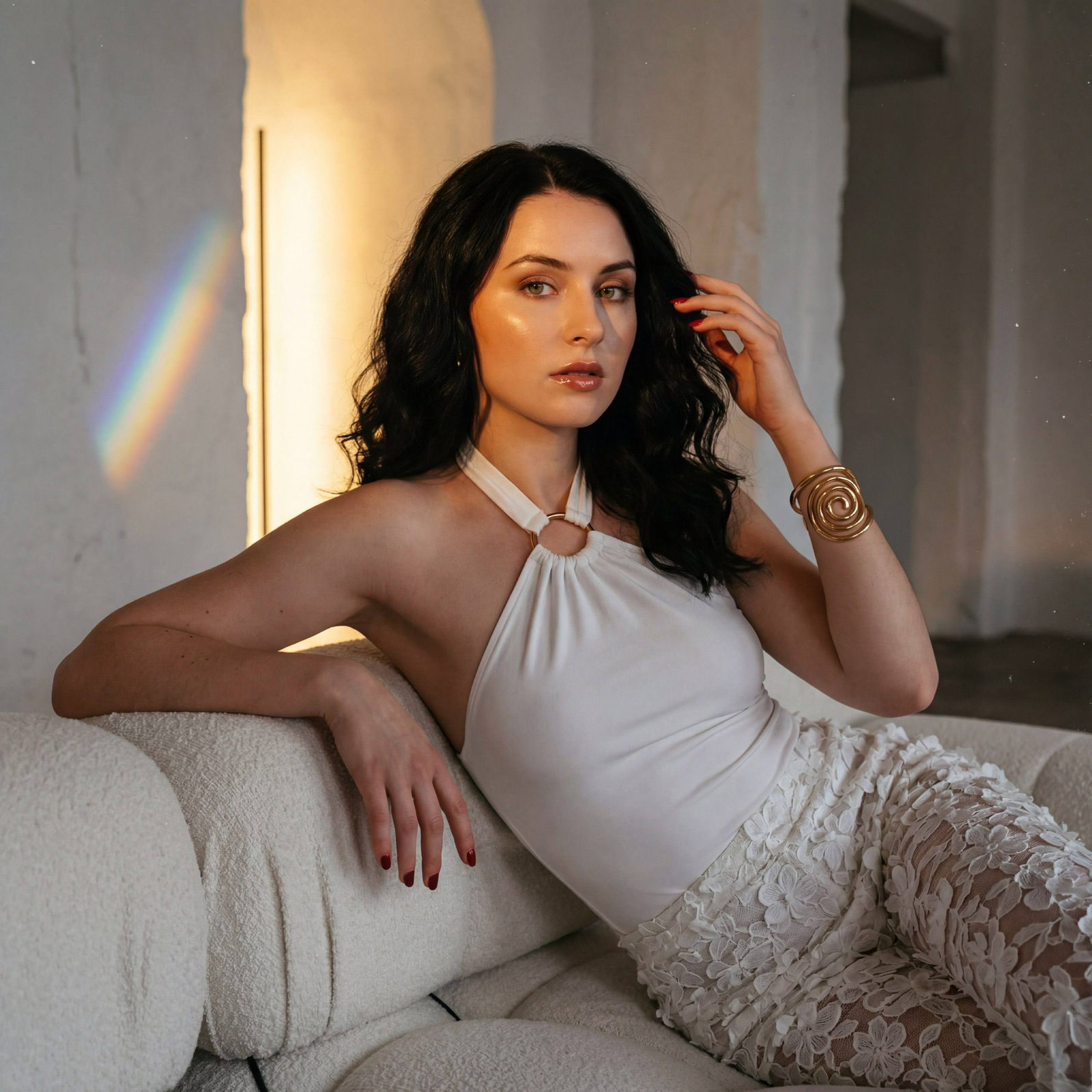 An editorial portrait depicting a woman on a luxurious modular sofa, styled with voluminous curls and high-shine lips in a golden light.