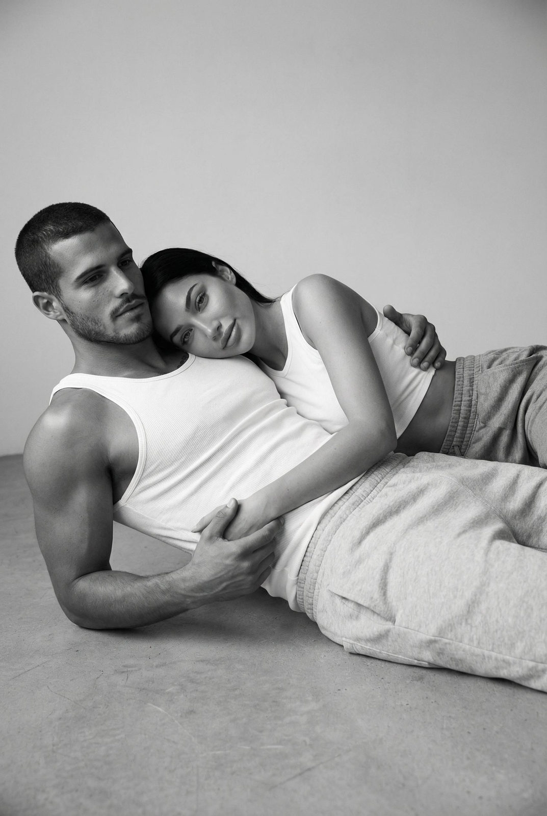 A couple in a studio setting, one lying on the other, showcasing calm body language and soft side lighting.
