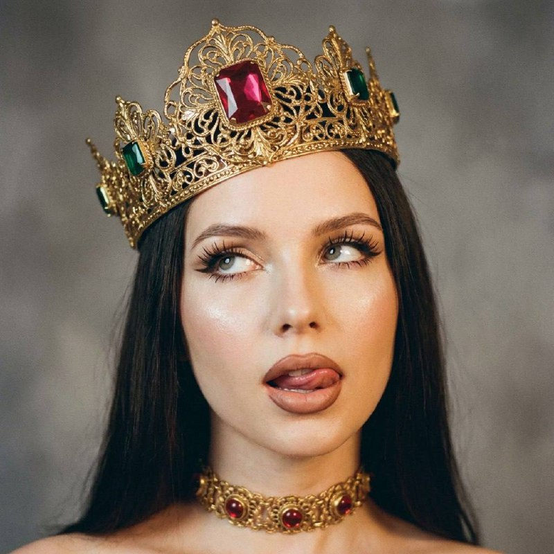 A model poses provocatively with a vintage golden crown and chic choker, soft diffuse lighting accentuating her bold makeup.