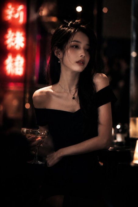 Close-up portrait of a woman in a black dress holding a golden cocktail in a neon-lit bar, with soft bokeh background.