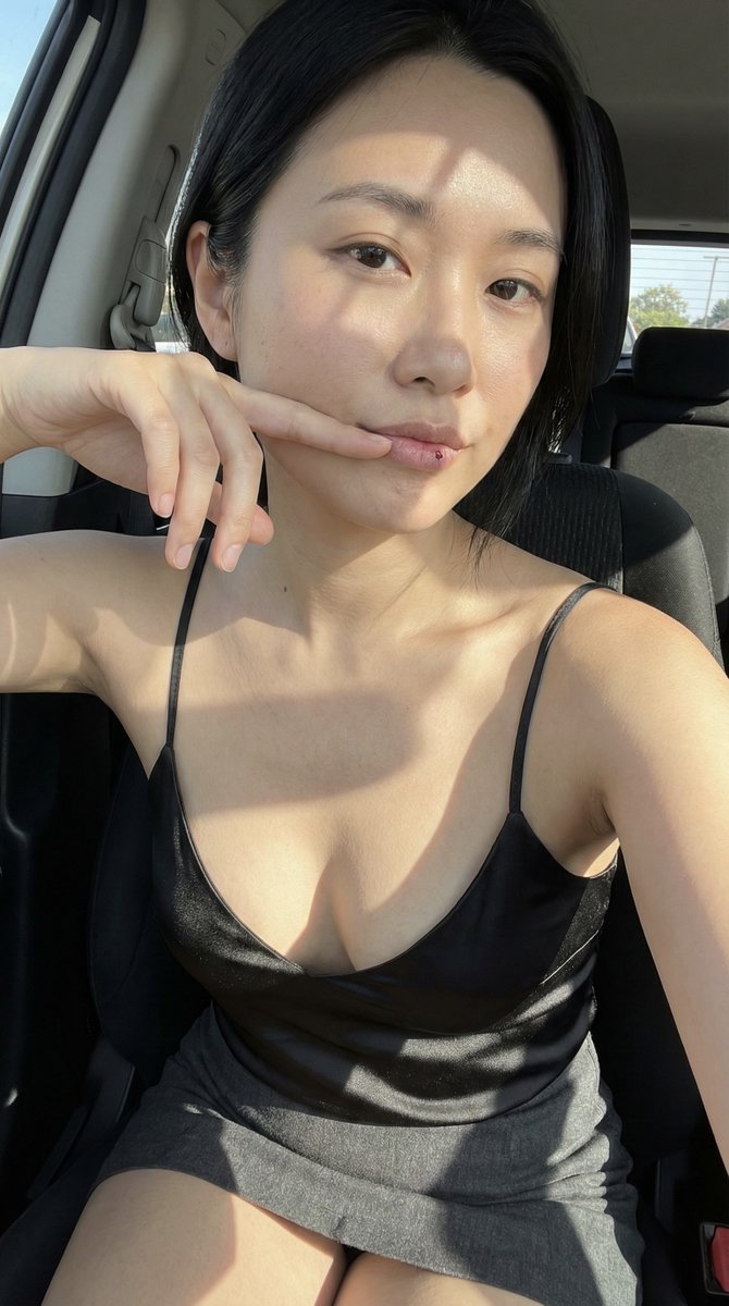 A woman in a parked car passenger seat, taking a candid selfie with sunlight stripes cutting across her chest and lips.