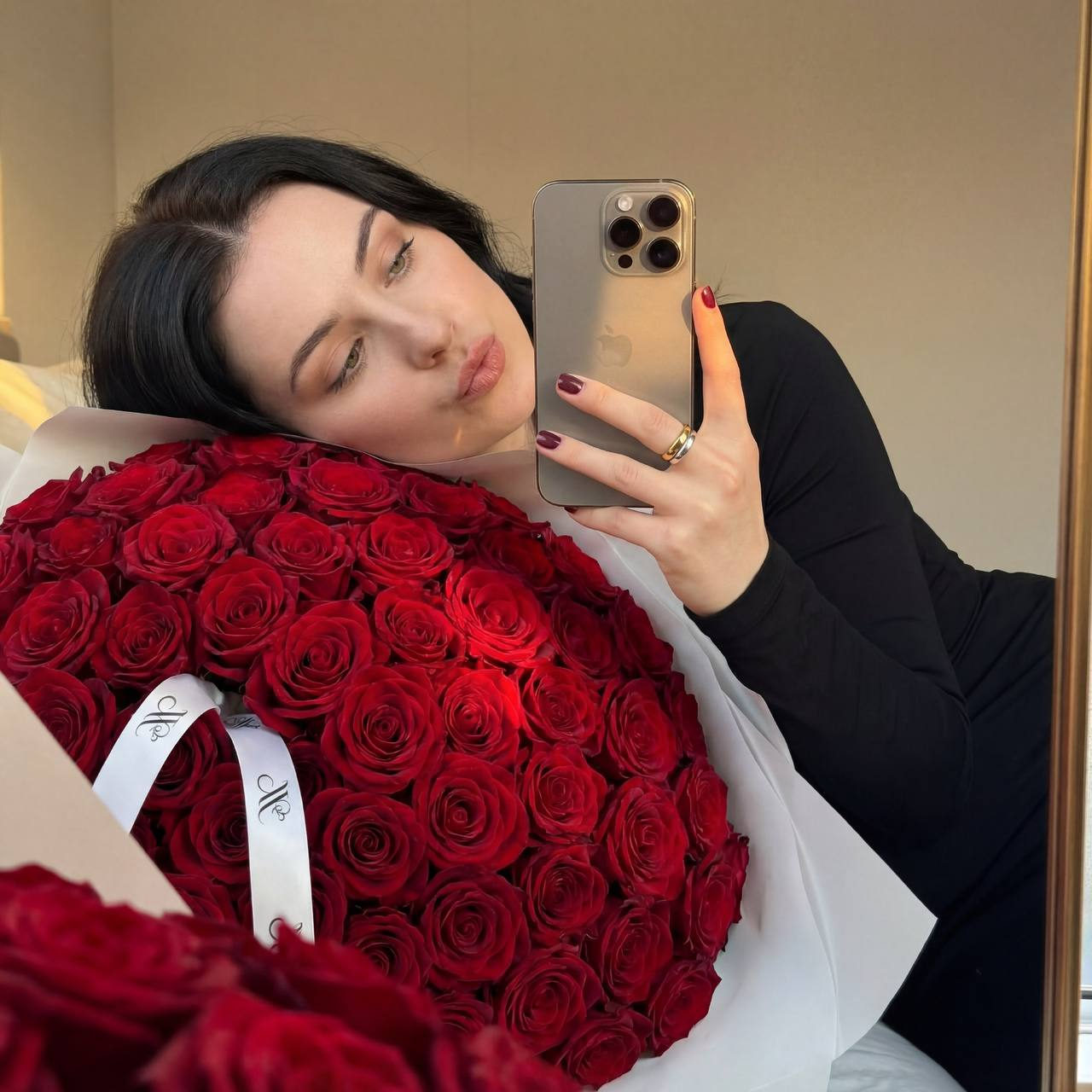 A cinematic mirror selfie featuring a person reclining on a flat surface, surrounded by deep red roses in full bloom, capturing a luxurious moment.