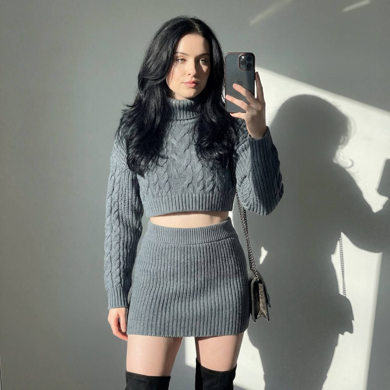 A fashionably posed woman with voluminous dark hair taking a selfie indoors, featuring sunlight casting dramatic shadows.
