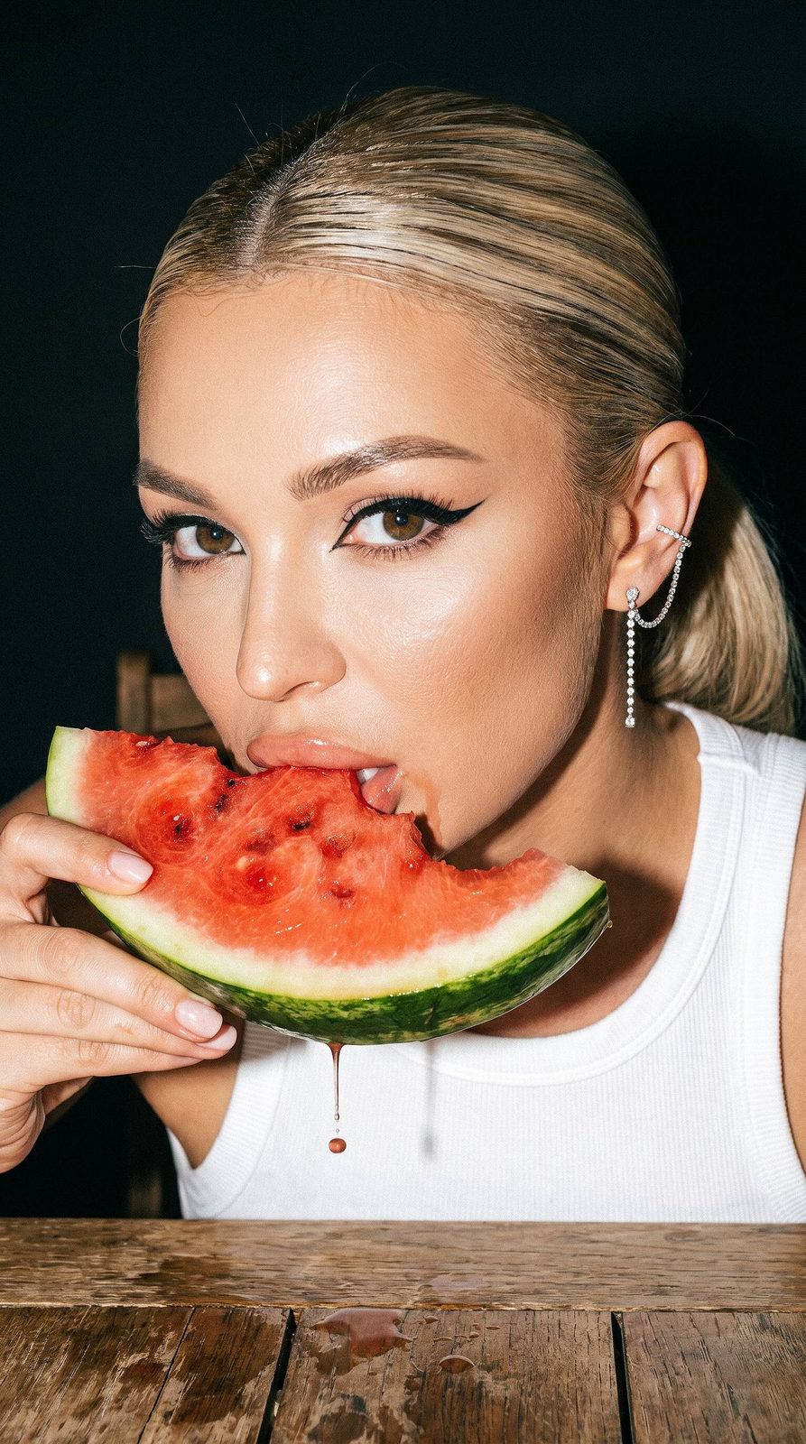 Close-up portrait of a woman holding a watermelon slice, juice dripping from her hand, featuring a diamond ear cuff earring.