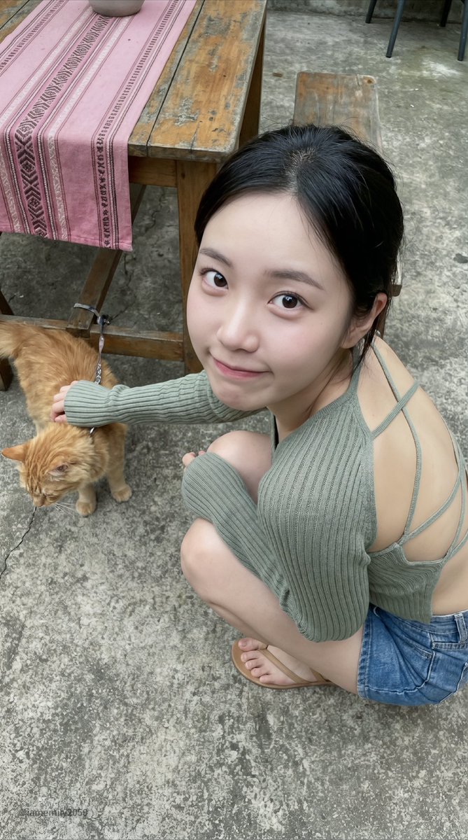 Young Asian woman with a playful expression, crouching on a patio, interacting with a ginger cat.