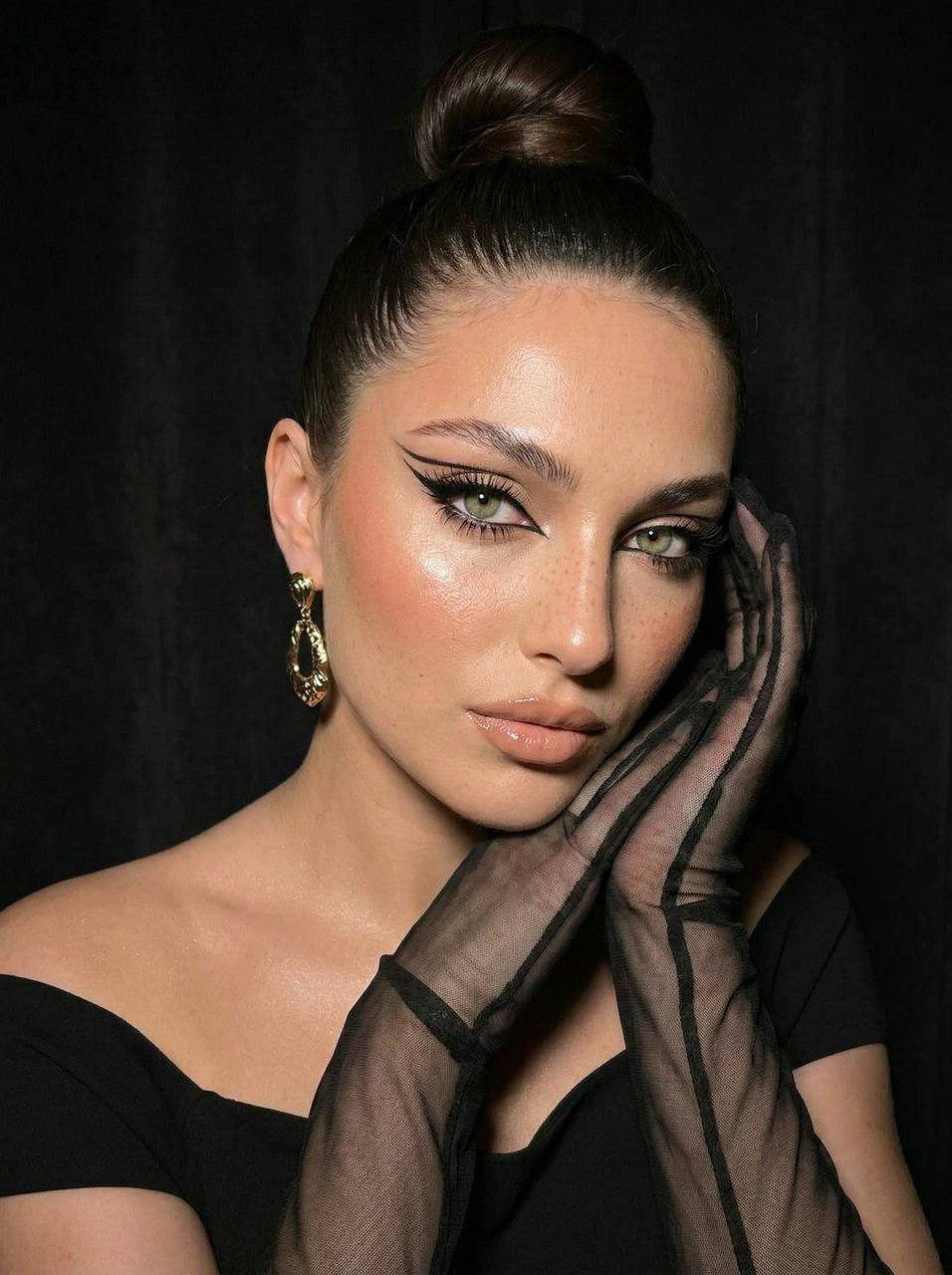 Close-up of a girl with vibrant makeup and an elegant hairstyle in a glamour portrait style, soft focus on the dark background.