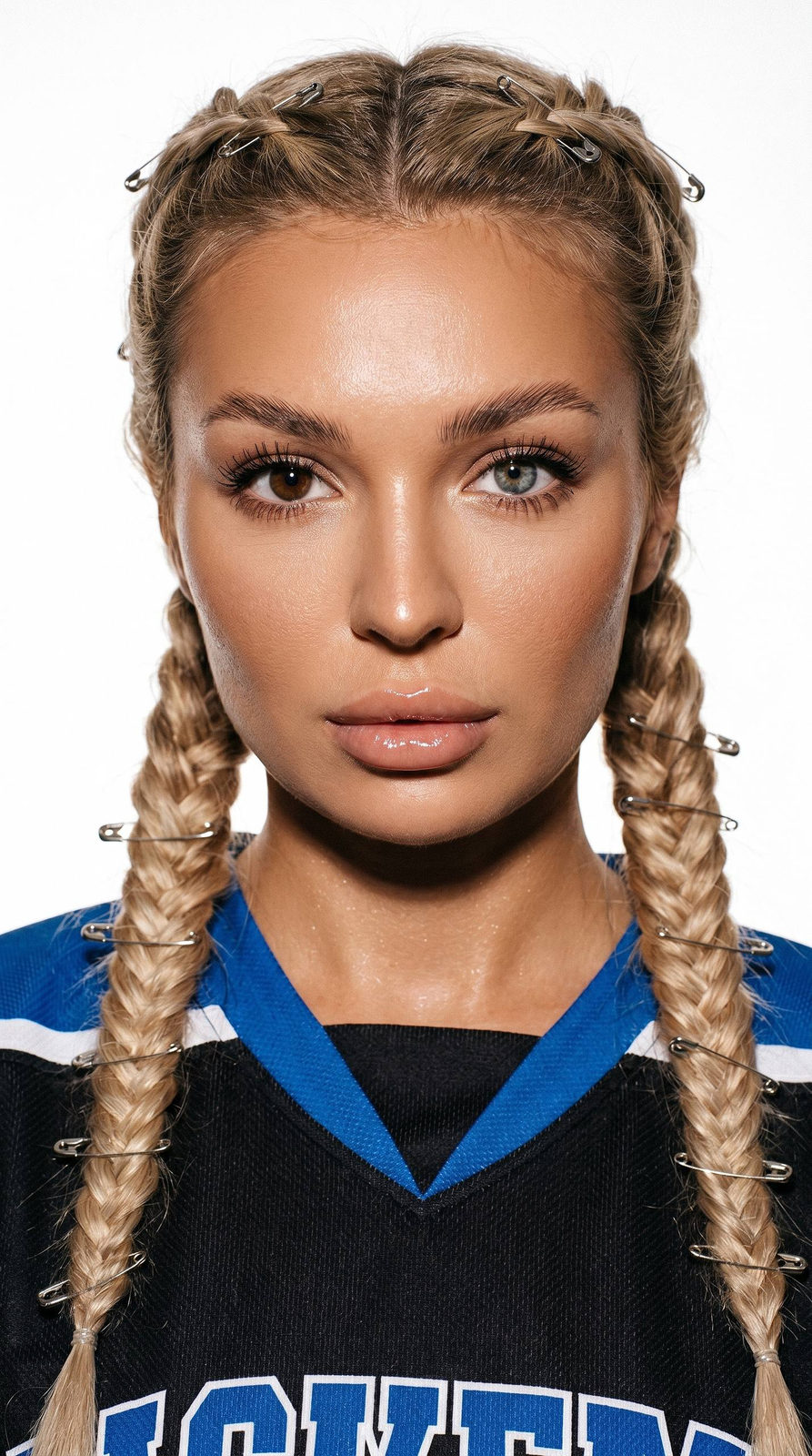 Close-up shot of a girl in a black and blue hockey jersey, standing with braided hair and a cinematic grain effect on a white background.