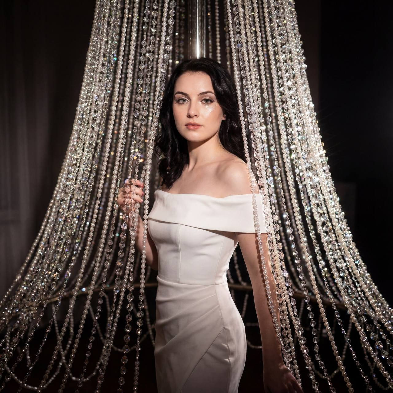Elegant woman in an evening gown surrounded by shimmering crystals and pearls, illuminated by soft, glamorous light.