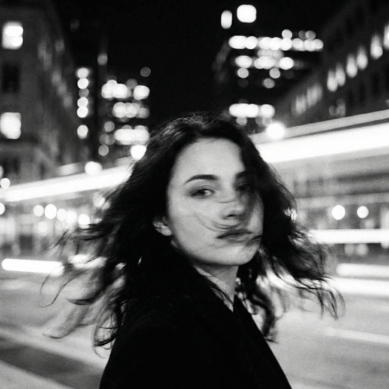 A ghostly woman in the city with long hair flowing while turning her head, surrounded by luminous bokeh lights.