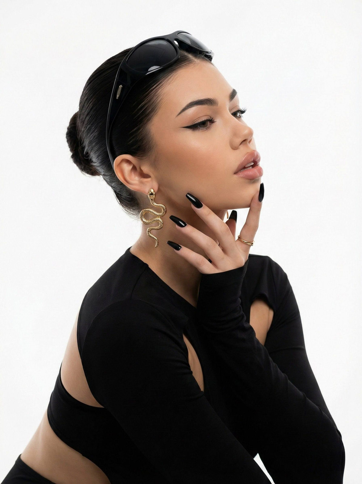 Close-up glamour portrait of a woman in a fitted black cutout dress with elegant accessories against a clean white background.