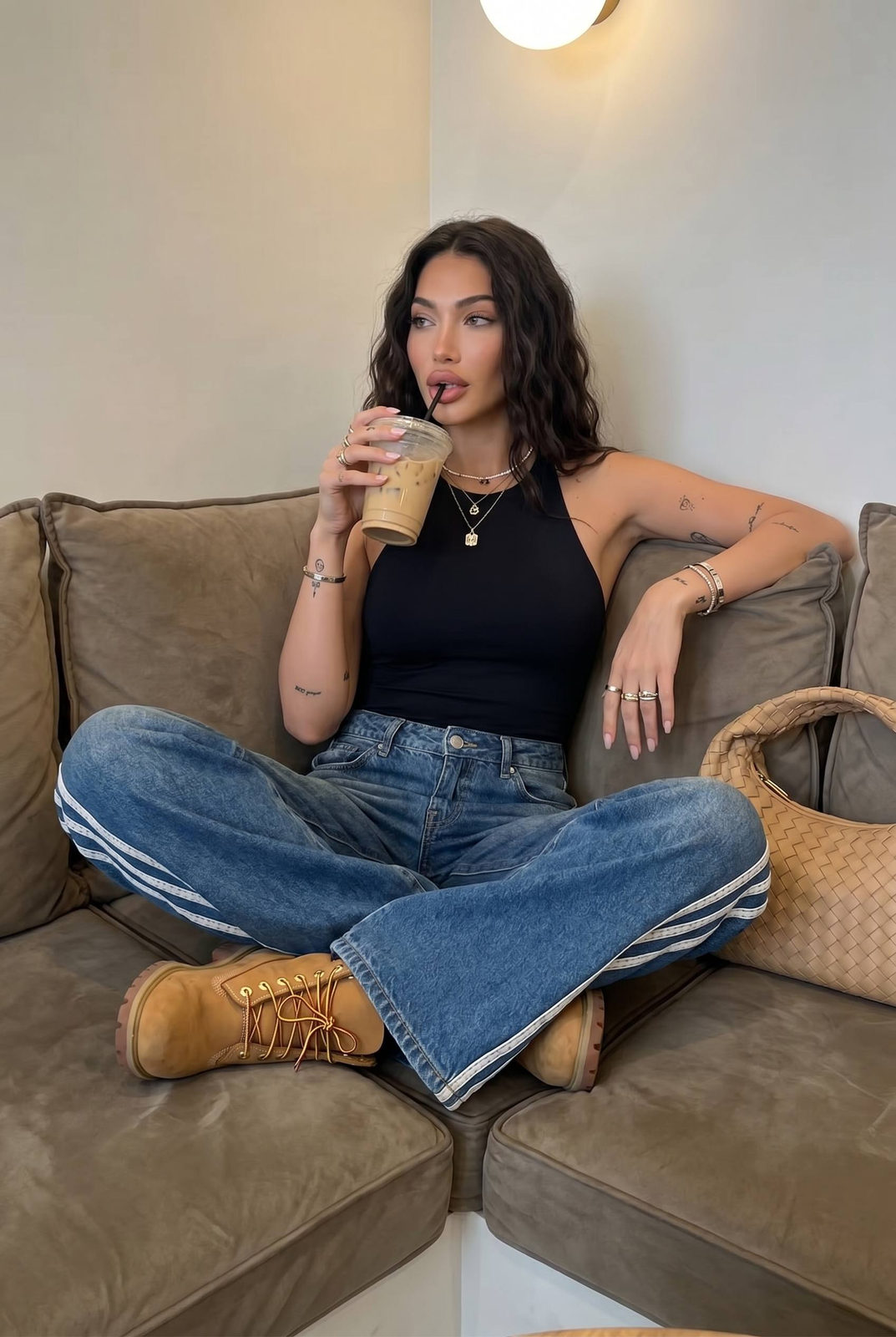 A woman sitting on a plush sofa, sipping an iced beverage while showcasing a relaxed pose.