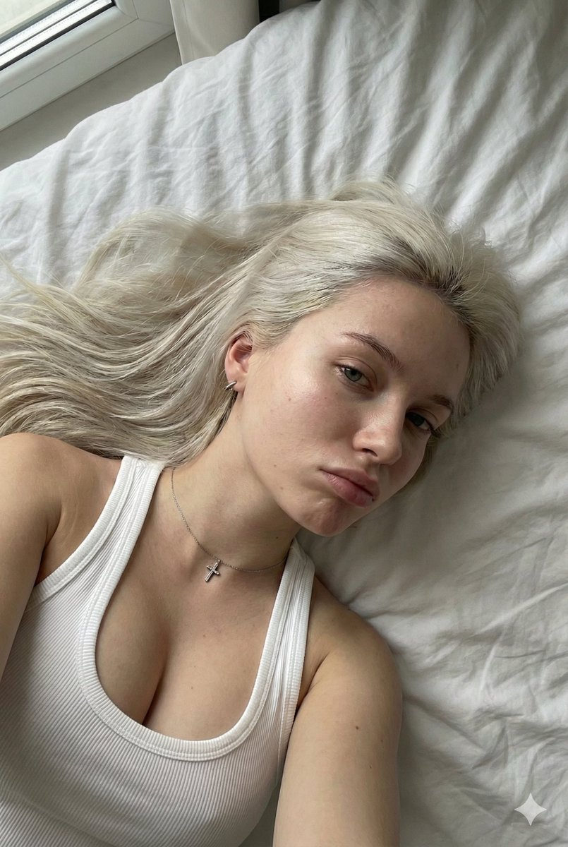 A young woman with platinum blonde hair lying on a bed, soft lighting accentuating her delicate features.