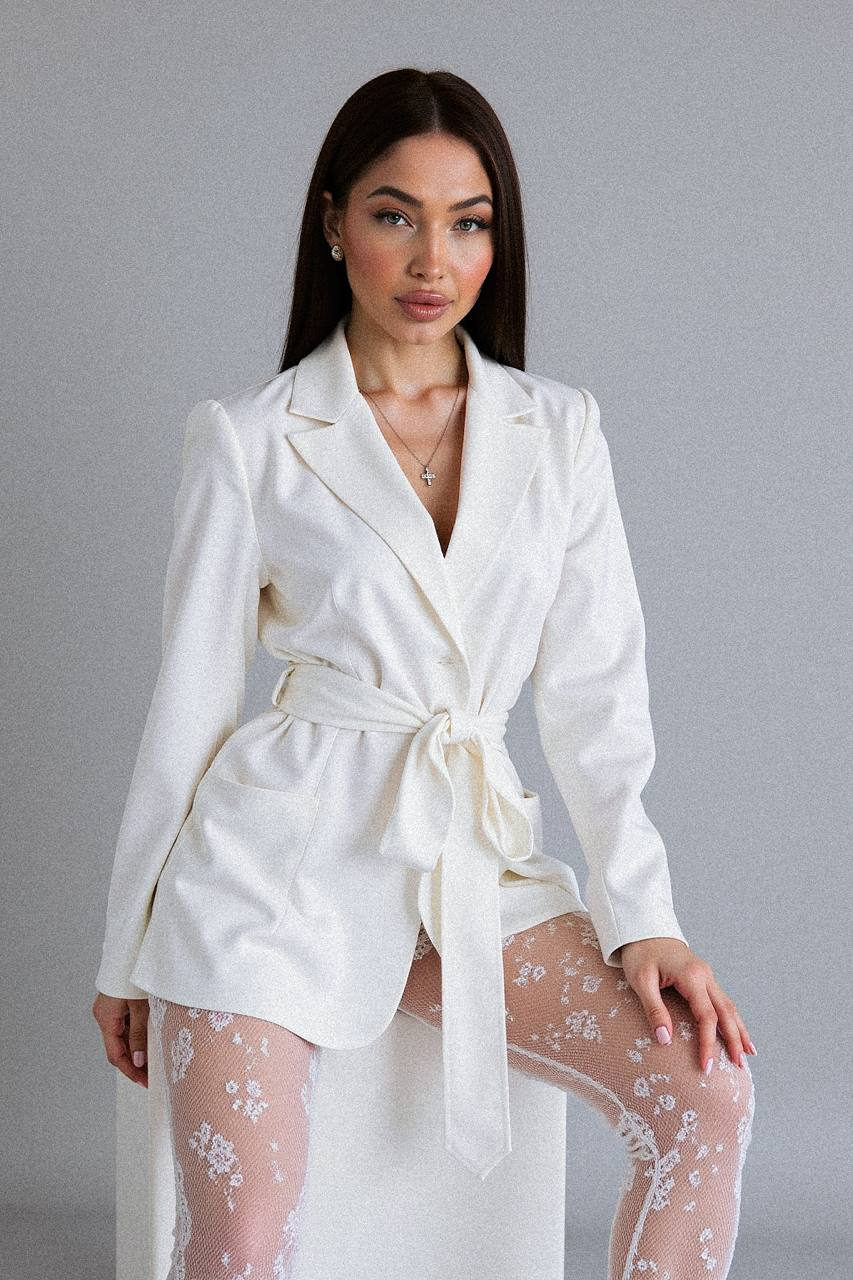 A confident model in an elegant blazer and sheer lace tights against a soft gray background, showcasing delicate shadows and smooth textures.