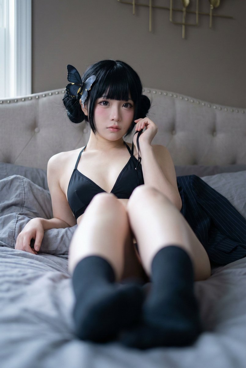 A woman reclines on a bed, wearing a black triangle halter top, with jet black hair styled in twin buns and a blue-black butterfly hair clip.